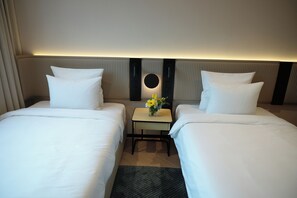 A hotel room with two beds, a small table with a vase of flowers, and a wall-mounted mirror.