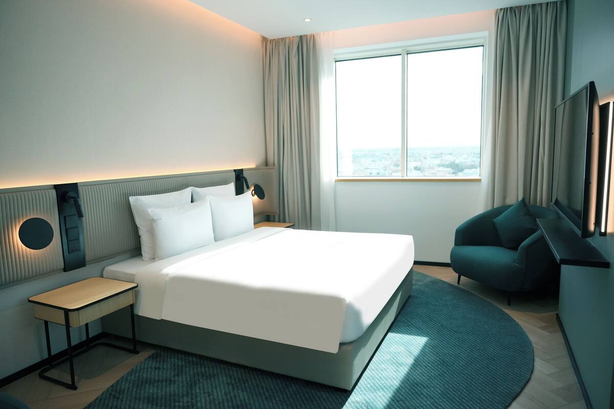 Une chambre d’hôtel moderne, dotée d’un grand lit, de tables de chevet, d’une télévision et offrant une vue sur la ville.