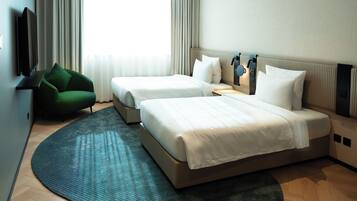 Habitación de hotel con dos camas, un televisor de pantalla plana, un sillón verde y un ventanal con cortinas.