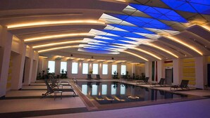 A spacious indoor swimming pool with a modern ceiling design and multiple windows.