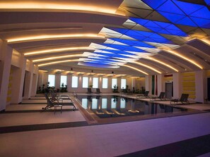 A spacious indoor swimming pool with a modern ceiling design and multiple windows.