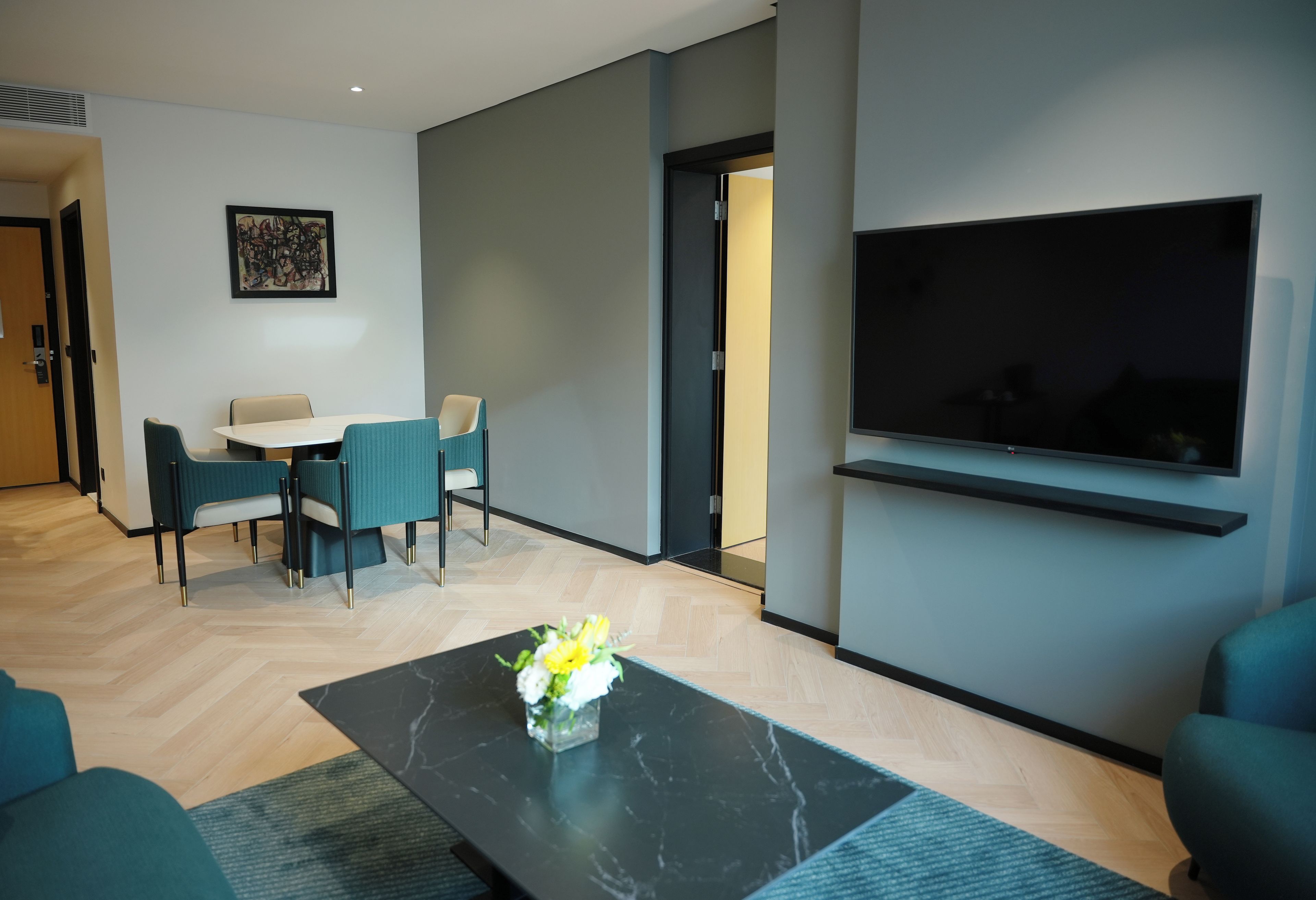 Uma sala moderna com área de jantar, uma TV de tela plana na parede e uma mesa de centro com flores.