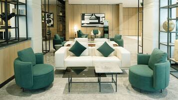 Un hall moderno con un sofá blanco, sillones verdes y una mesa de centro de vidrio.