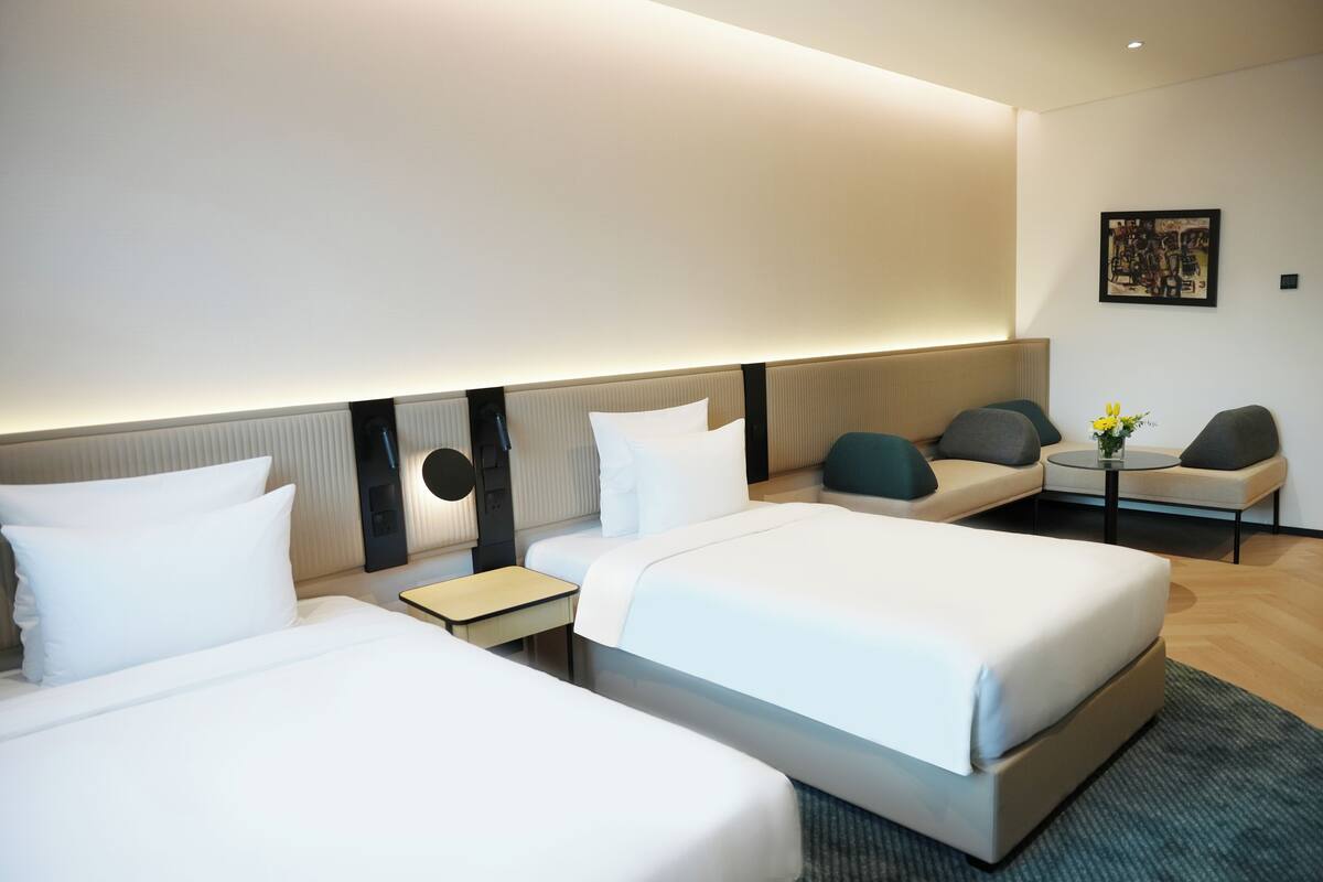 Une chambre d’hôtel avec deux lits, un canapé, une petite table et une œuvre d’art accrochée au mur.