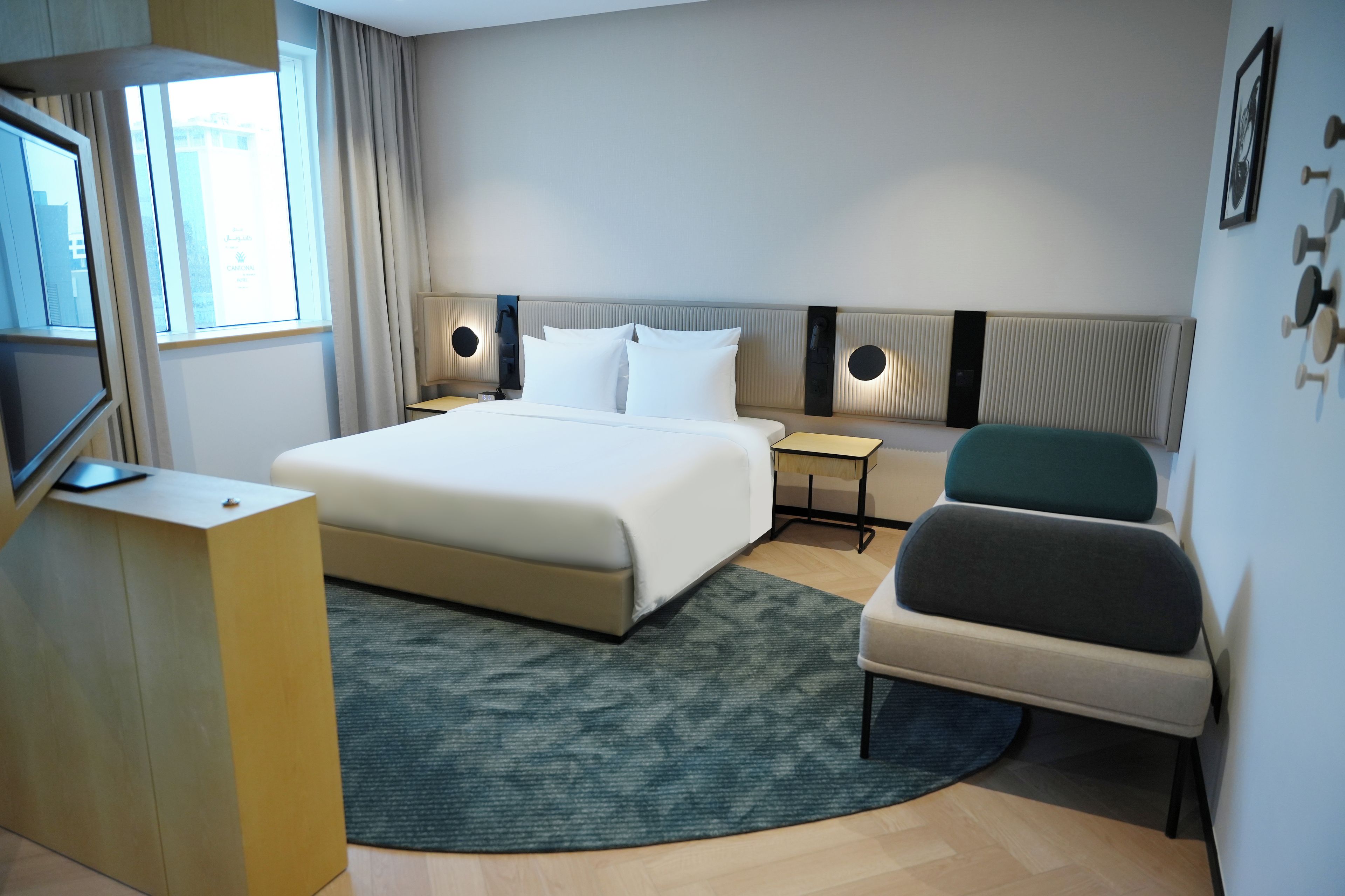 Quarto de hotel com cama, mesas de cabeceira, uma cadeira, televisão e janela com cortinas.
