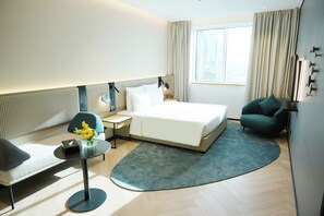 Habitación de hotel con cama, mesita de noche, lámpara, silla y vistas a la ciudad por la ventana.
