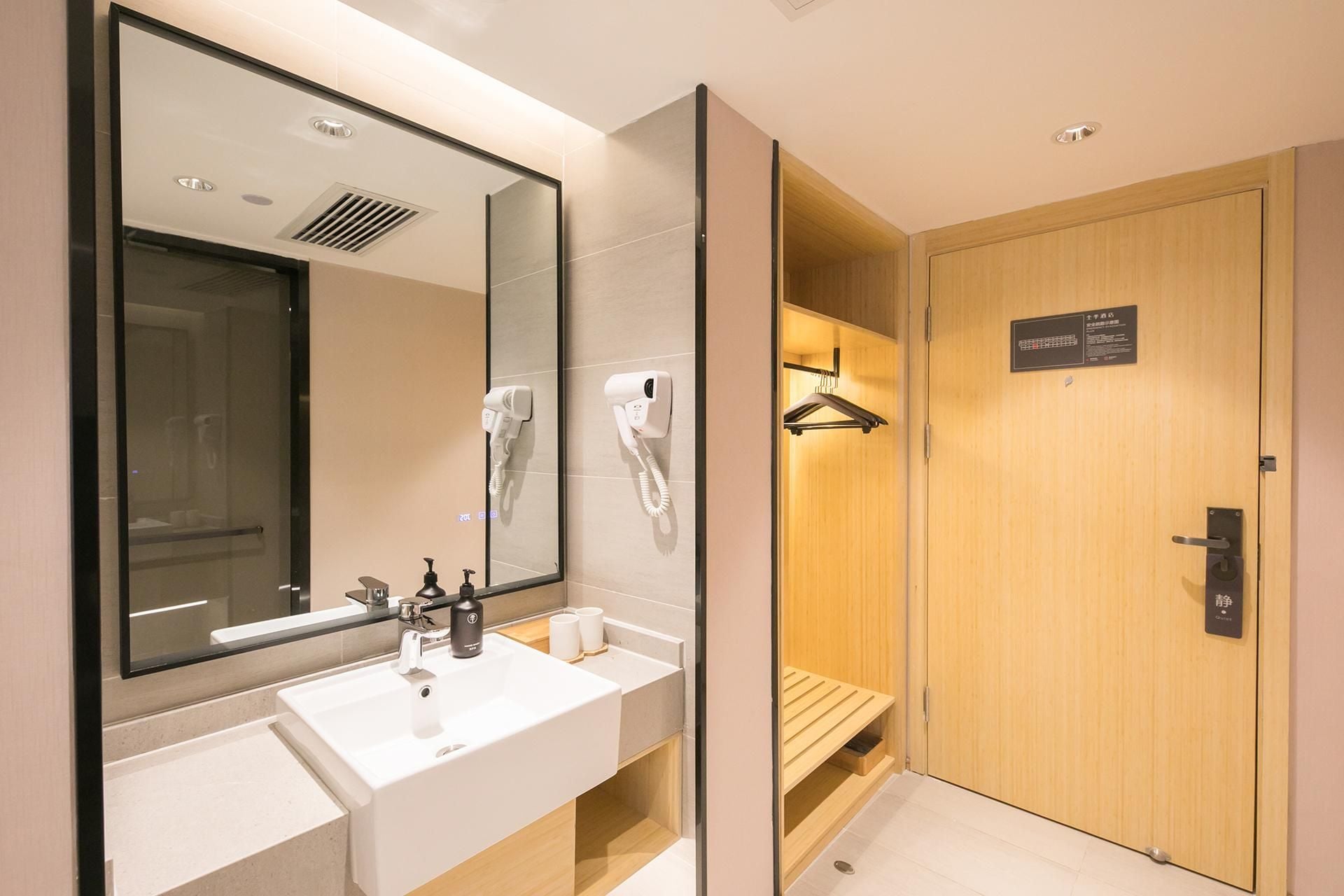 A modern bathroom with a large mirror, two sinks, a towel rack, and a wooden door leading to a shower area.