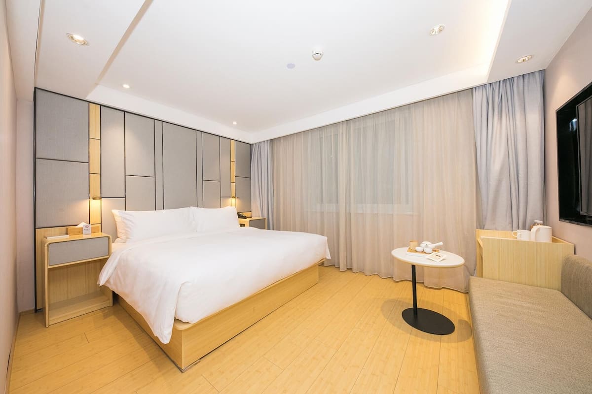 Une chambre d’hôtel moderne avec un grand lit, des tables de chevet, une petite table ronde et un téléviseur.