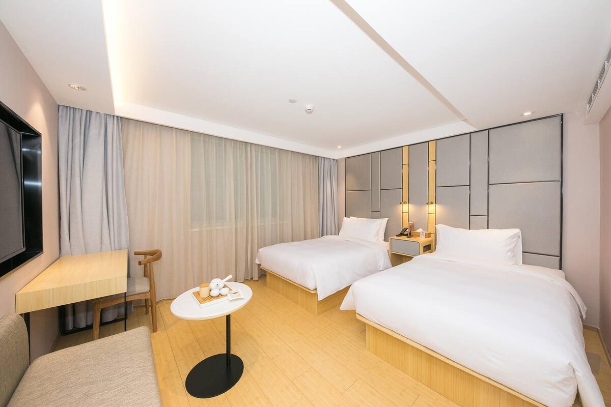 Une chambre d’hôtel avec deux lits, une petite table, un téléviseur et un grand miroir.