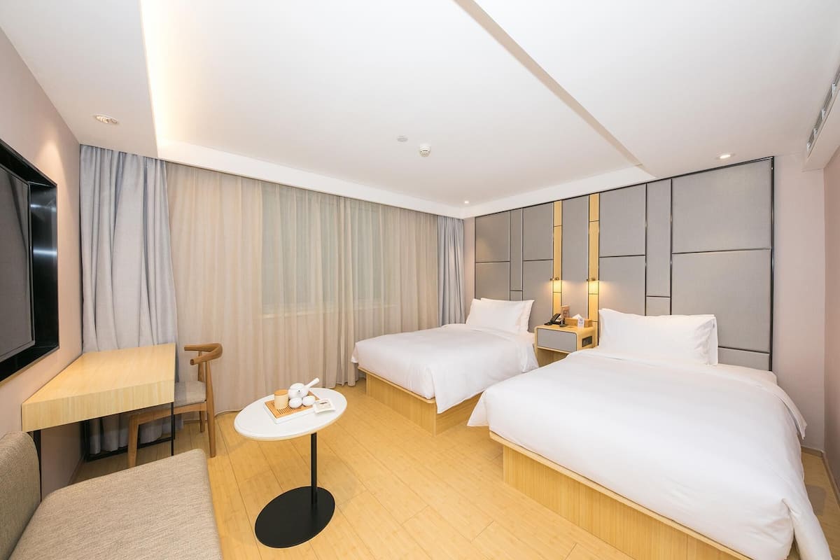 Hotellihuone, jossa on kaksi sänkyä, pieni pöytä, televisio ja suuri peili.