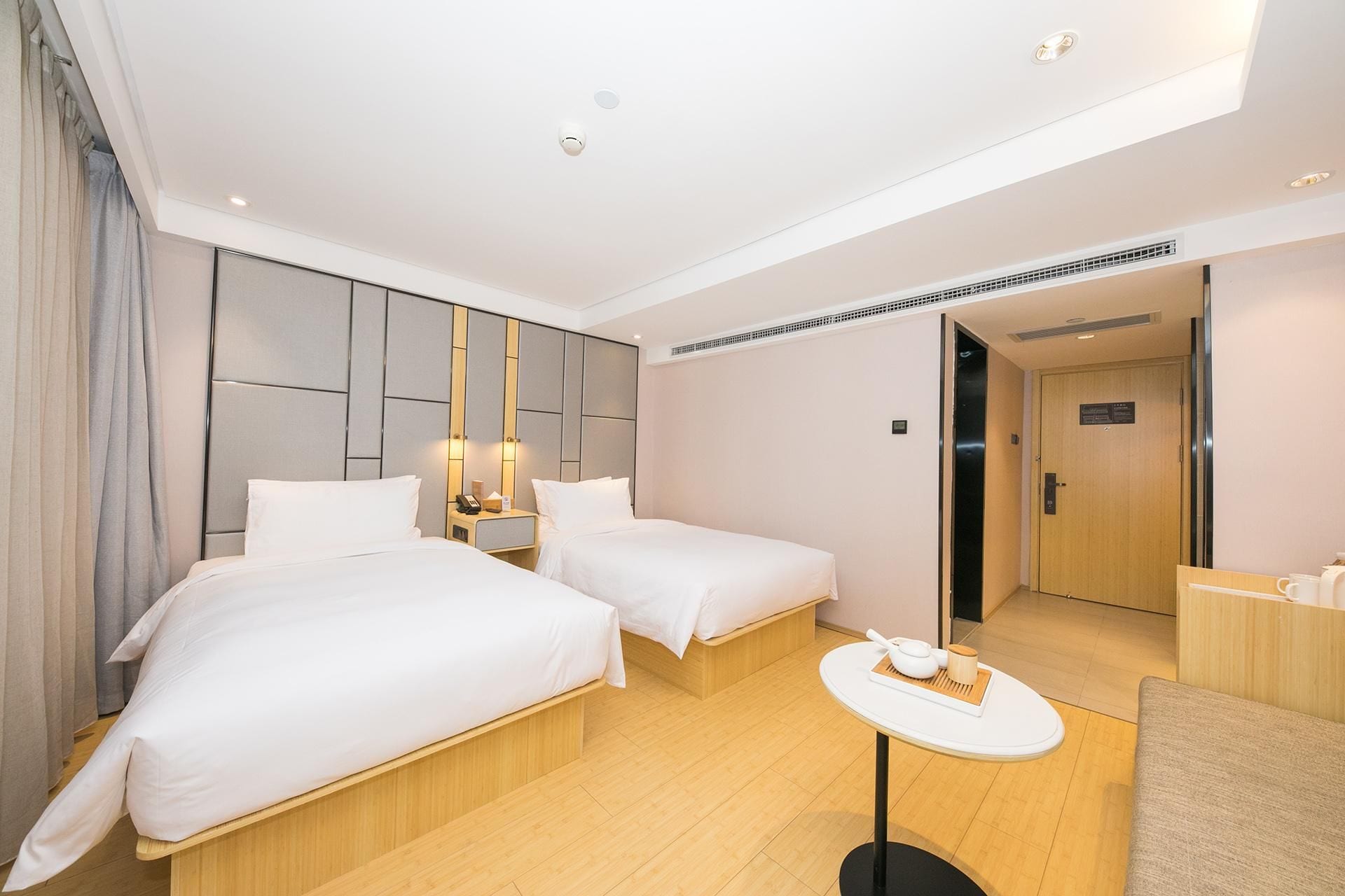 A hotel room with two beds, a small table, and a door leading to a bathroom.