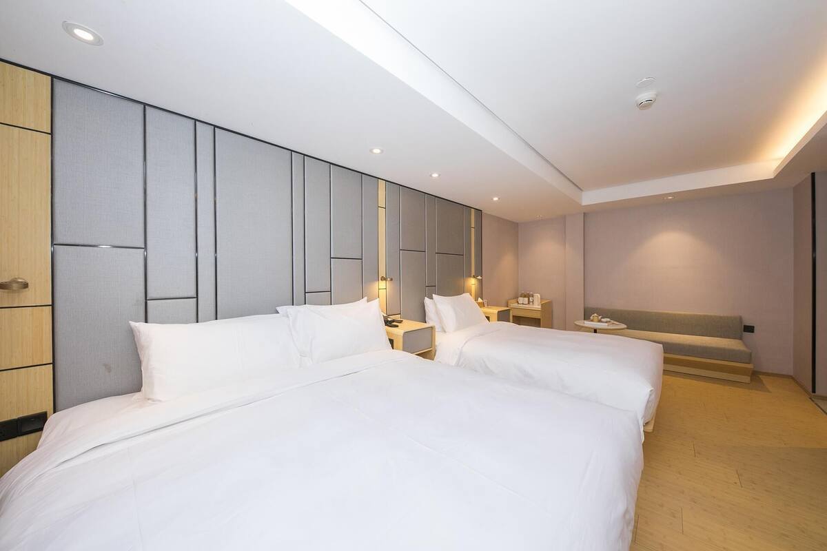 Une chambre d’hôtel avec deux lits, un canapé, une petite table et un téléviseur fixé au mur.