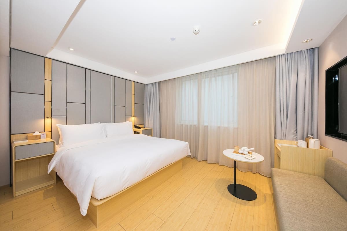 Une chambre d’hôtel moderne avec un grand lit, des tables de chevet, une petite table ronde et un téléviseur.