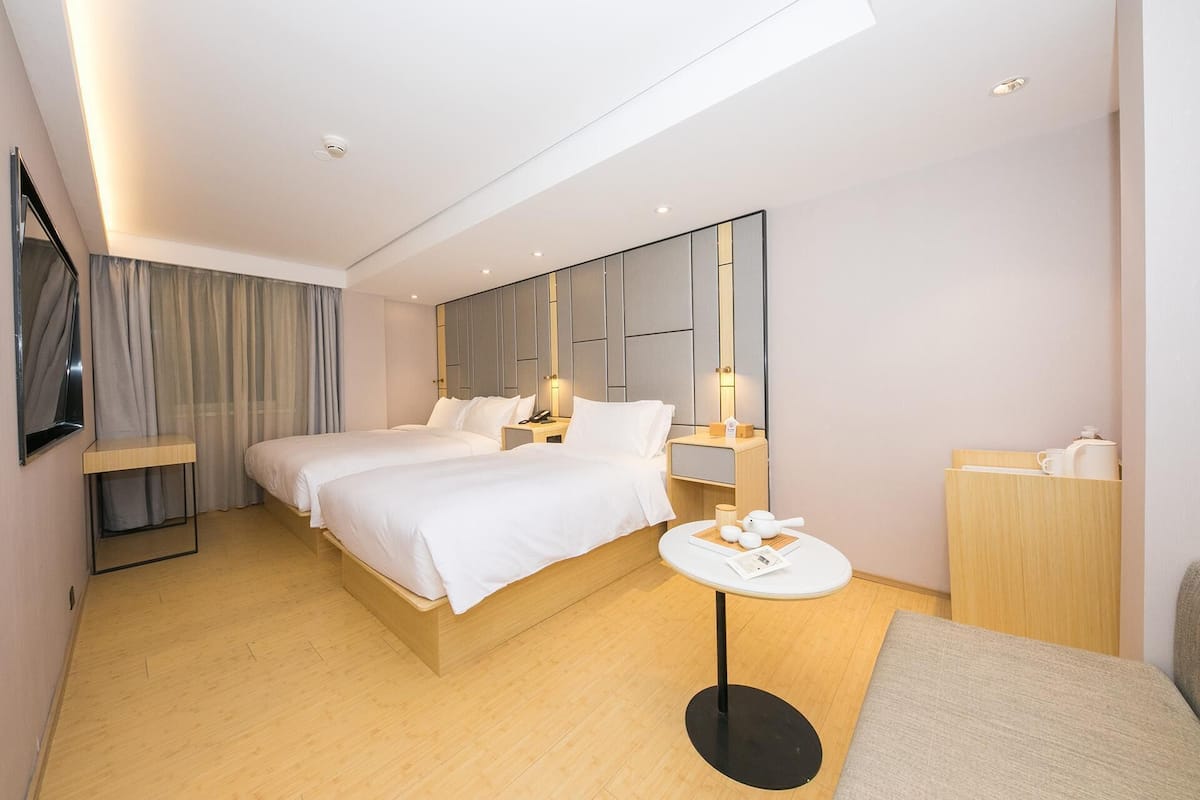 Une chambre d’hôtel avec deux lits, une table de chevet, une table ronde, un miroir et une armoire.