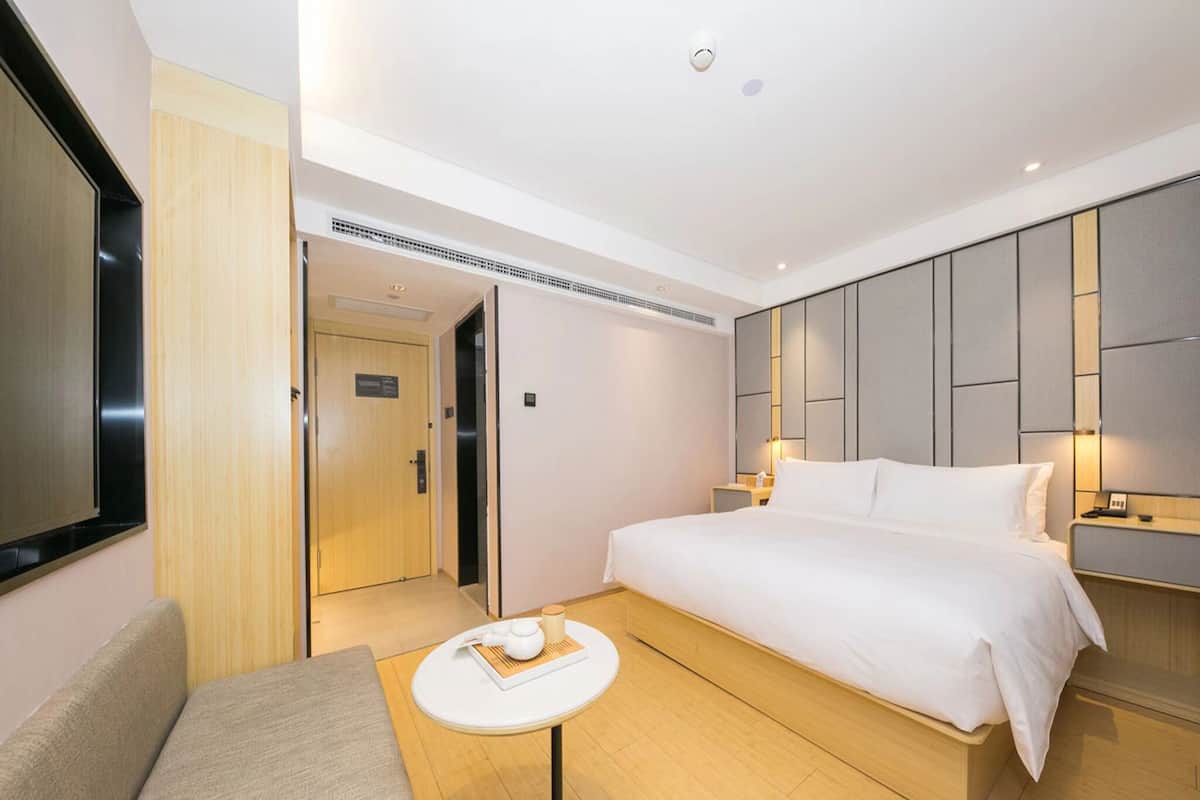 Une chambre d’hôtel avec un lit, une petite table sur laquelle se trouvent une tasse et un livre, un canapé et un téléviseur.
