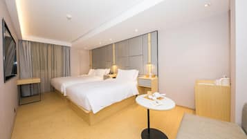 A hotel room with two beds, a bedside table, a round table, a mirror, and a wardrobe.