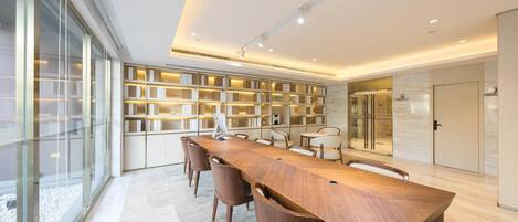 A modern dining area with a long wooden table, several chairs, and a bookshelf filled with books.