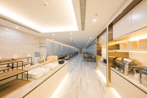Un hall d’hôtel moderne avec un long comptoir d’accueil, un espace salon et une cuisine visible sur la droite.