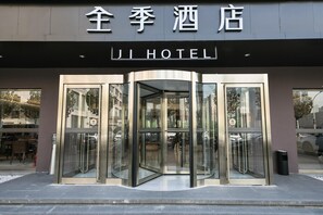 L’entrée d’un hôtel, avec une porte tournante et une enseigne au-dessus indiquant « JI HOTEL ».