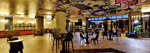 Un espacio interior amplio con techo alto, que presenta un mural, varios arreglos de asientos y ventanas grandes con vistas al exterior.