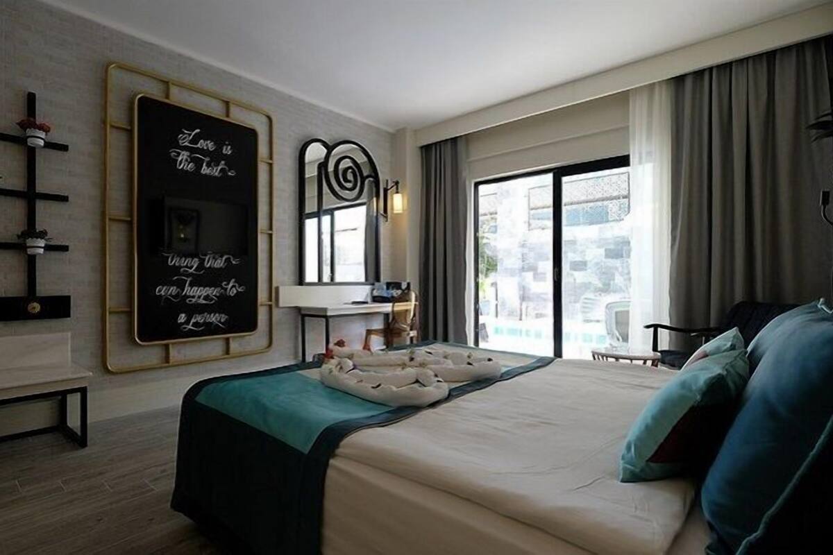 Ein Hotelzimmer mit Bett, Schreibtisch, Stuhl, Fenster und einem Wandspiegel.
