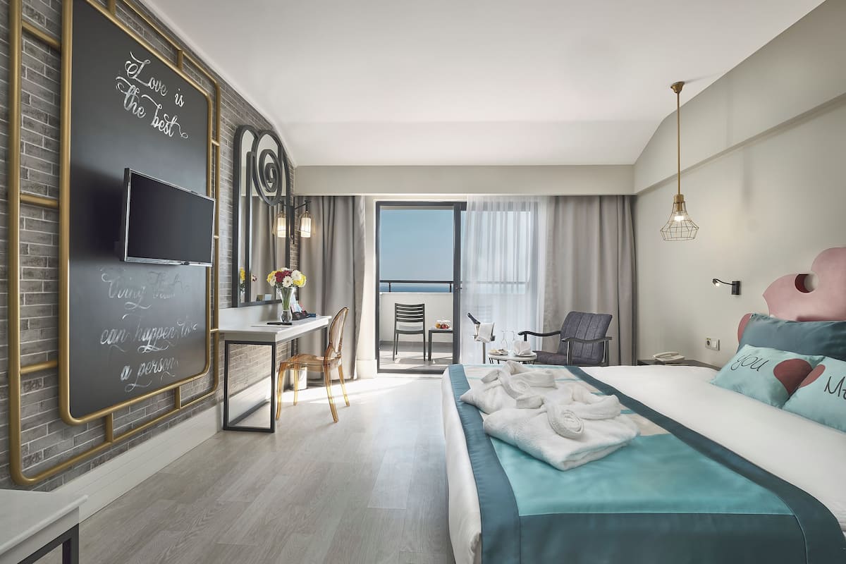 Ein modernes Hotelzimmer mit Bett, Schreibtisch, Stuhl, Fernseher und Balkon.