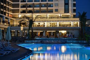 Un hotel con piscina, mobiliario exterior y un edificio de varios pisos con balcones.
