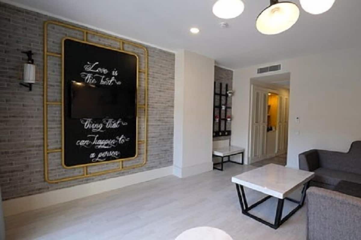 Ein modernes Wohnzimmer mit einer großen Tafel an der Wand, einem grauen Sofa, einem weißen Couchtisch und einer Tür zu einem weiteren Raum.