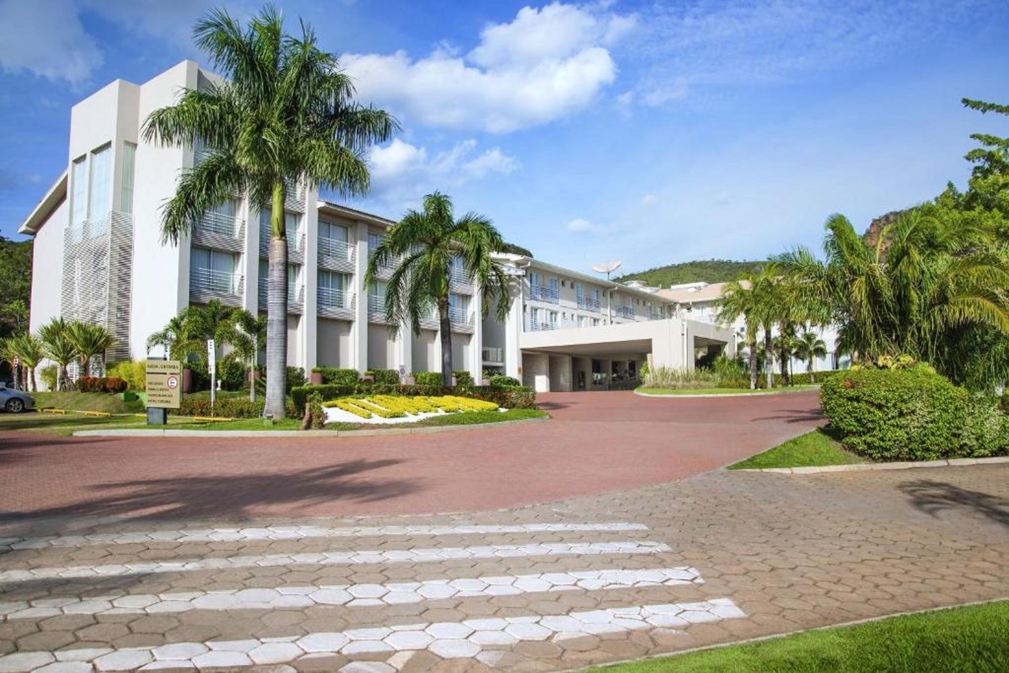A modern hotel with a central courtyard, palm trees, and a clear sky.