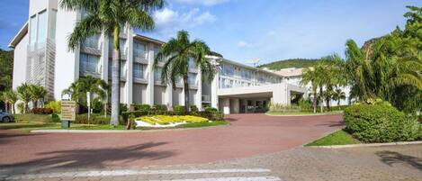 A modern hotel with a central courtyard, palm trees, and a clear sky.