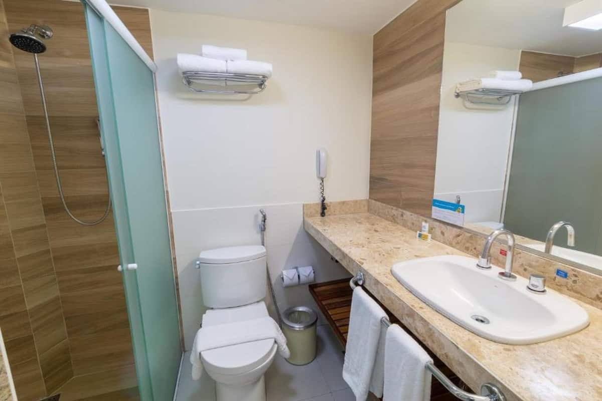 Un baño con ducha, dos inodoros, un lavabo y un espejo.