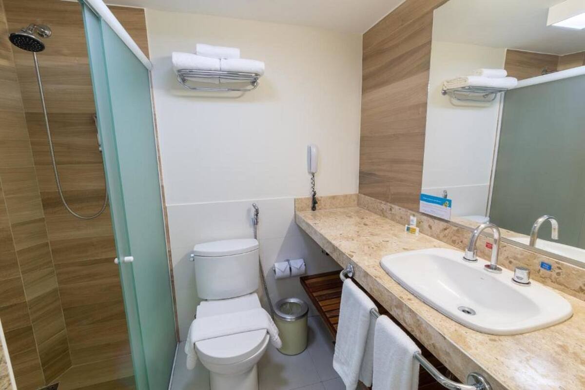 A compact bathroom with a shower, two toilets, a sink, and a mirror.