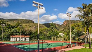 An outdoor tennis court with a net, surrounded by greenery and hills.