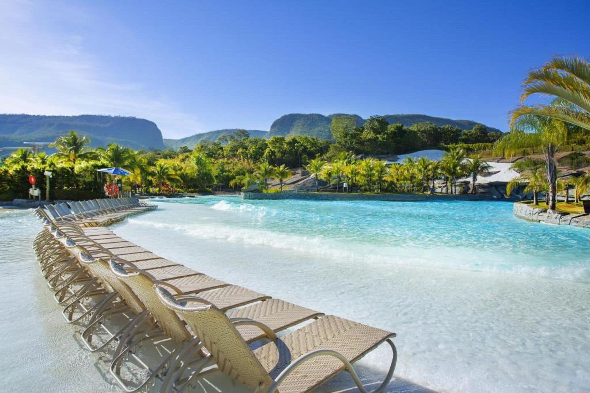 A pool with clear water, surrounded by lounge chairs and palm trees.