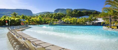 Una piscina con agua cristalina, rodeada de sillas de descanso y palmeras.