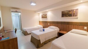 A hotel room with three single beds, a wooden desk, and a small bedside table.
