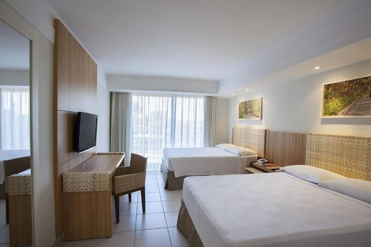 Una habitación de hotel con dos camas, un escritorio, un televisor y obras de arte en las paredes.