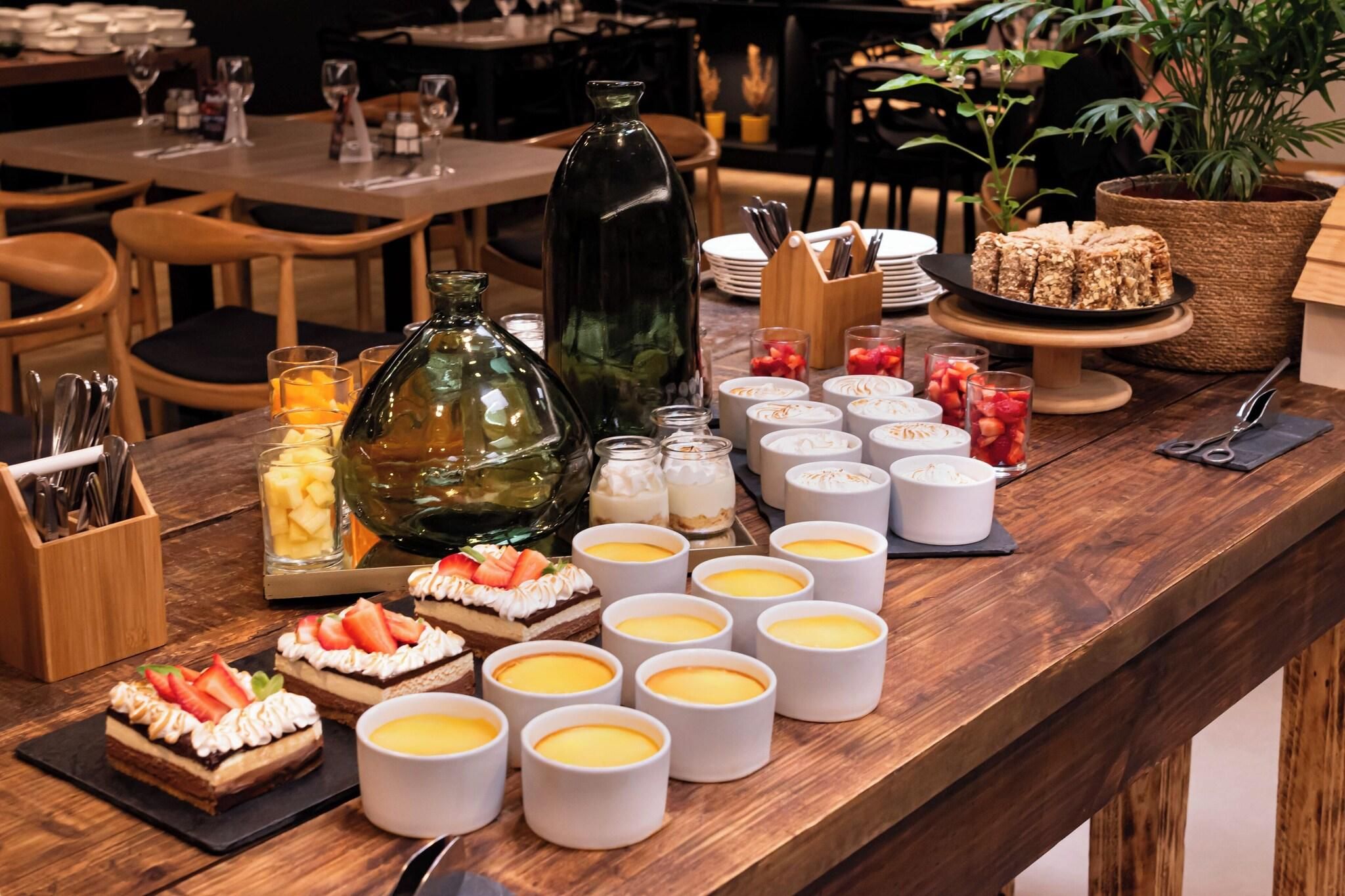 A buffet table with various desserts, including cakes and fruit tarts, and several white cups, likely containing beverages.