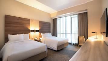 Quarto de hotel com duas camas, uma mesa, uma televisão e uma janela com cortinas.