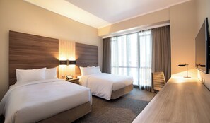 Habitación de hotel con dos camas, un escritorio, un televisor y una ventana con cortinas.