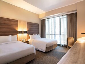 Una habitación de hotel con dos camas, un escritorio, una silla, una lámpara y un ventanal con cortinas.