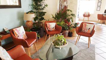 A modern lounge area with leather armchairs, a glass coffee table with a plant centerpiece, and various potted plants.