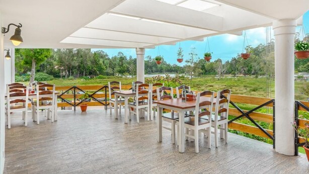 An outdoor seating area with wooden tables and chairs, a white ceiling, and hanging planters.