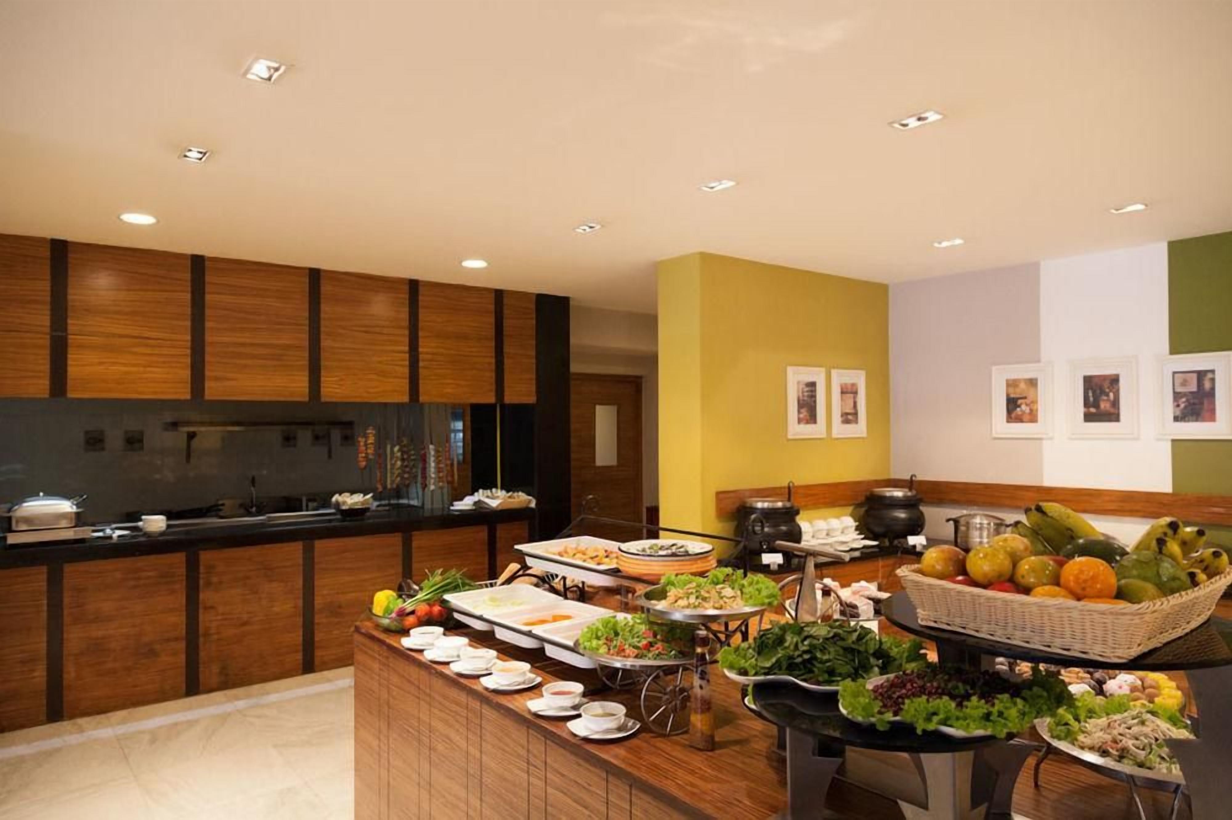 A buffet with various food items and a kitchen area with wooden cabinets and a stove.