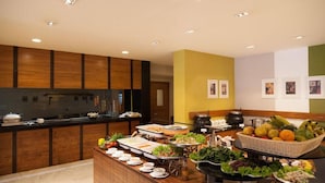 A buffet with various food items and a kitchen area with wooden cabinets and a stove.