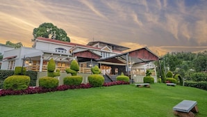 A hotel with a red roof, white walls, and a well-maintained garden with trimmed bushes and a lawn.