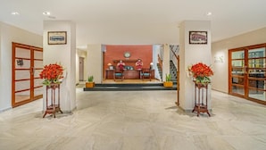 A hotel lobby with a reception desk, two flower stands, and a staircase leading to the upper floor.