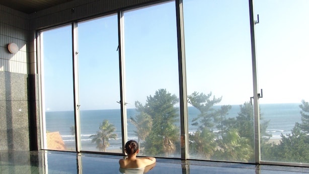 A person in a glass-enclosed infinity pool with a view of the ocean and palm trees. - ANA Holiday Inn Resort Miyazaki (Miyazaki)