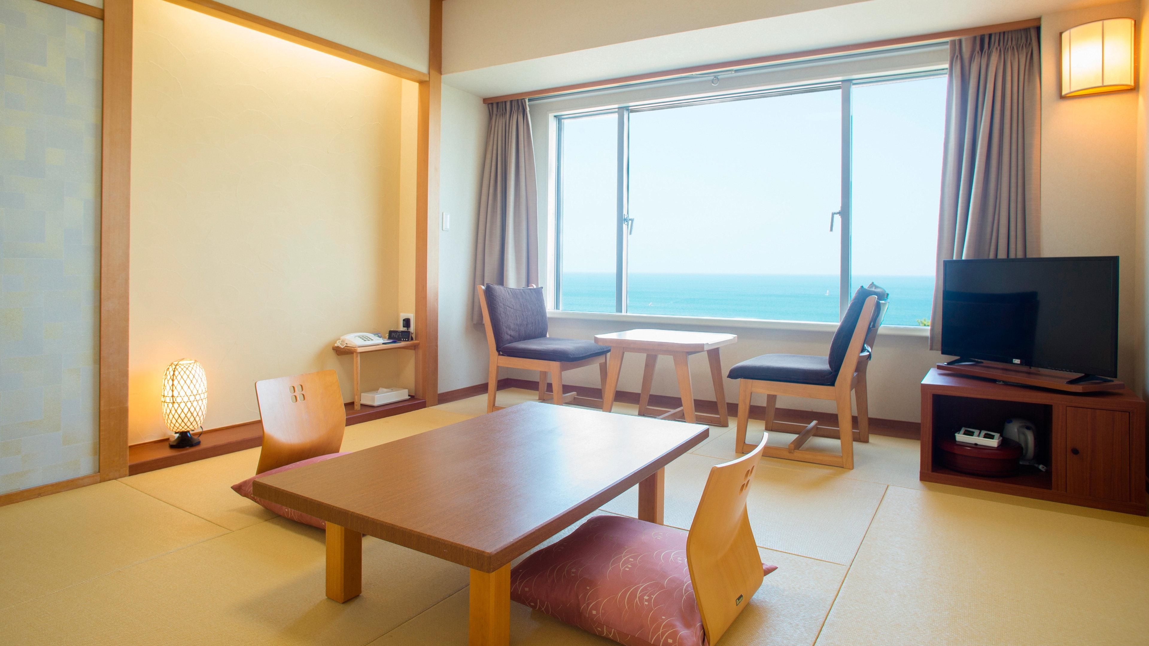 A hotel room with a wooden table, two chairs, a television, and a view of the sea.