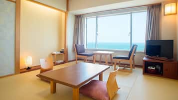 A hotel room with a wooden table, two chairs, a television, and a view of the sea.